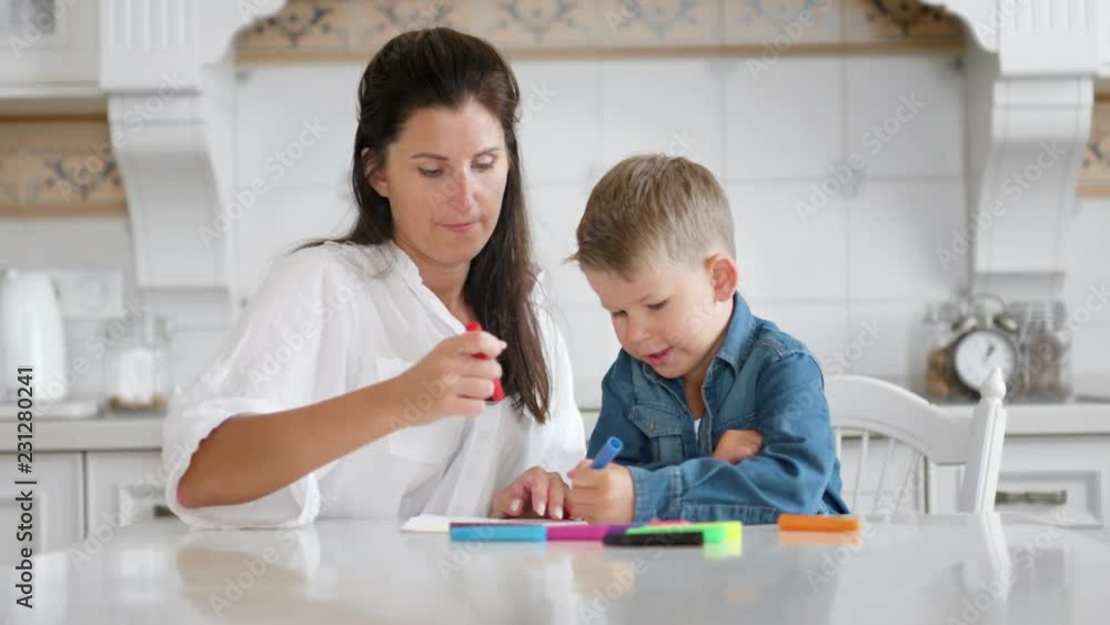 Beautiful mom and cute little son enjoying drawing picture together using multicolored felt-tip pen Beautiful mom and cute little son enjoying drawing picture together using multicolored felt-tip pen