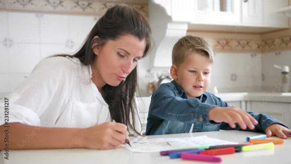 Mom and son draw image on paper together using multicolored felt-tip pen Mom and son draw image on paper together using multicolored felt-tip pen