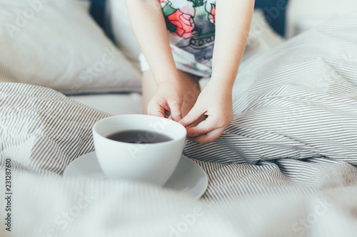 Bed maid-up with clean white pillows and bed sheets in beauty room. Morning breakfast with tea. Kid hold a cup. Close-up.