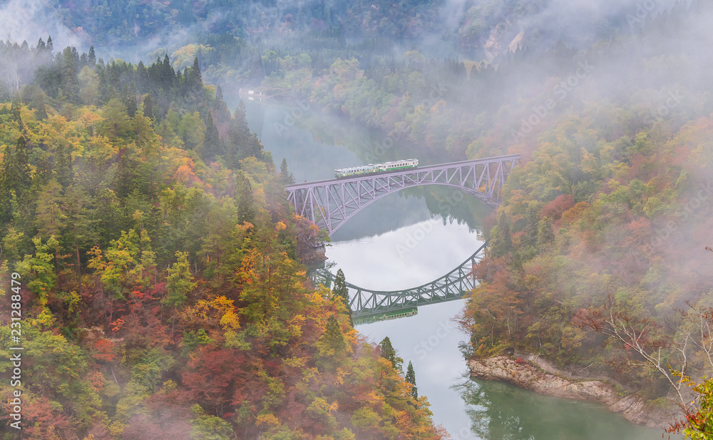 Fototapeta premium Train crossing the first bridge with surrounding beautiful autumn foliage and fog.