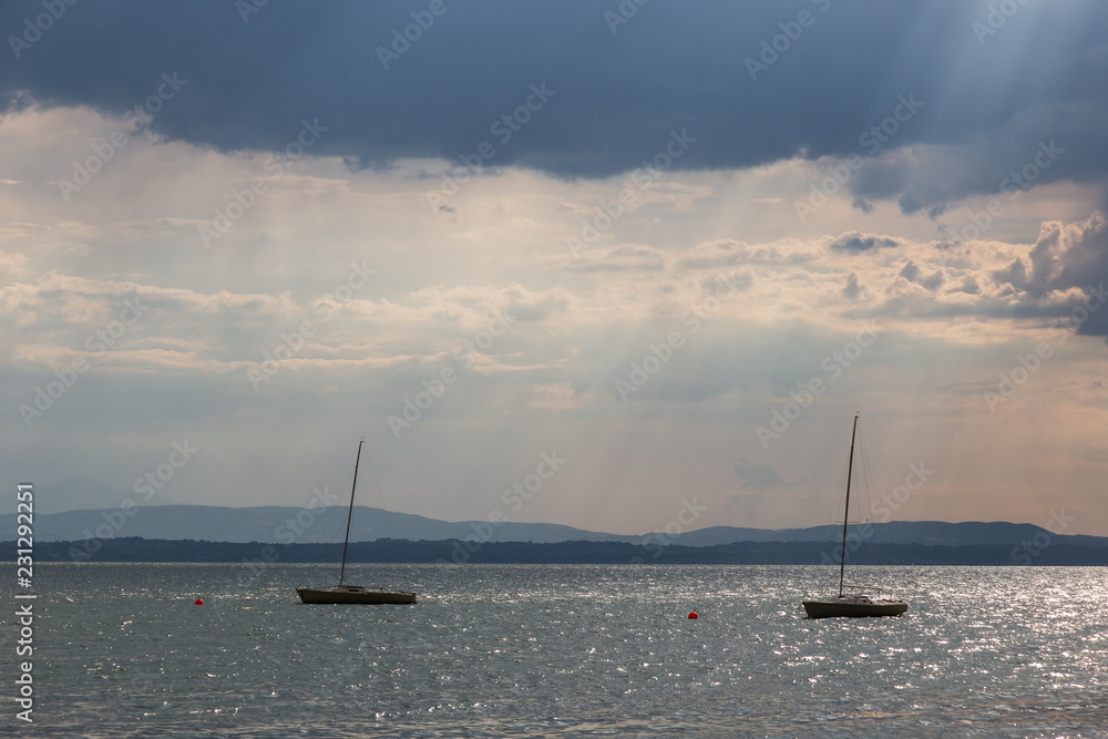 A couple of empty, little sailboat on a lake, beneath a moody sky with sun rays filtering through