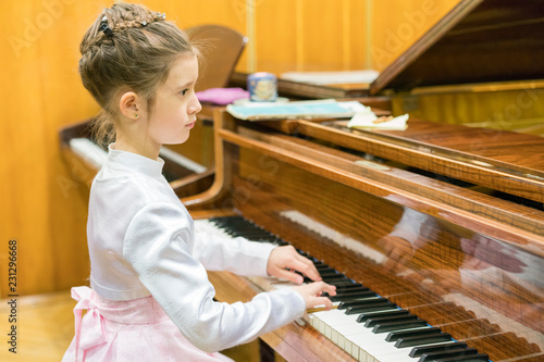 Quadro em tela A girl in a beautiful dress plays on a brown grand piano