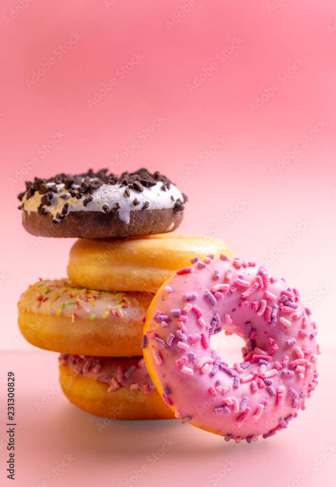 Pile of colorful donuts on pink background.
