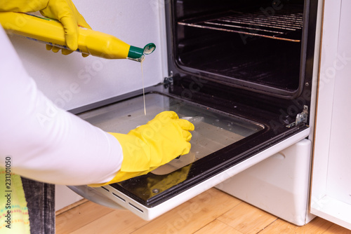 woman with an apron in yellow rubber gloves washing oven with a sponge