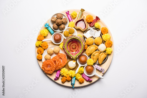 Diwali sweets arranged in a plate with diya and flowers