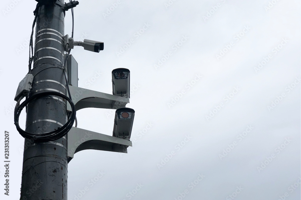 Cameras on the road pole. Three CCTV surveillance cameras on a pole. City cctv security surveillance camera system attached on the traffic light pole with gray sky background. Cameras on the road pole. Three CCTV surveillance cameras on a pole. City cctv security surveillance camera system attached on the traffic light pole with gray sky background.