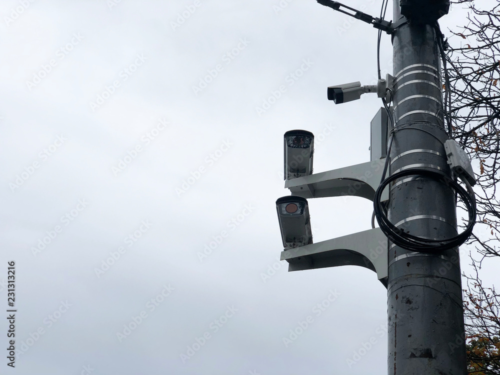Cameras on the road pole. Three CCTV surveillance cameras on a pole. City cctv security surveillance camera system attached on the traffic light pole with gray sky background. Cameras on the road pole. Three CCTV surveillance cameras on a pole. City cctv security surveillance camera system attached on the traffic light pole with gray sky background.