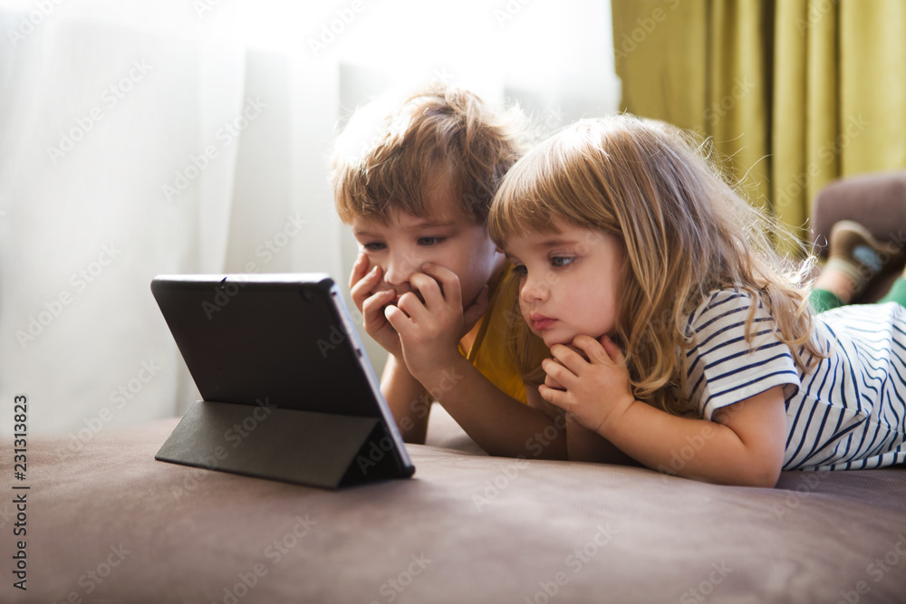 Two kids using tablet pc together relaxed at home.
Two kids using tablet pc together relaxed at home.