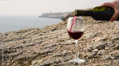 Red wine is poured into a glass on a background of rocky sea shore