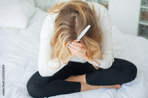 Positive pregnancy test. Young woman feeling depressed and sad after looking at pregnancy test result at home photo