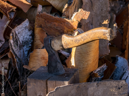 The axe stuck in a log in the yard about a woodpile on the street