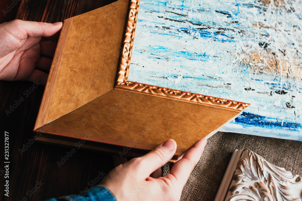 Fototapeta premium Choosing decorative frame for a painting. Woman's hands and sample of gold wooden frame.