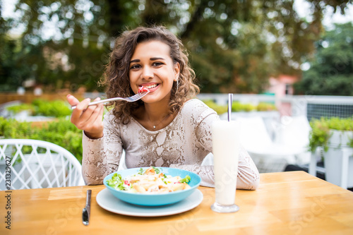 Portrait of a smiling mixed race curly american woman eating in cafe outdoors
