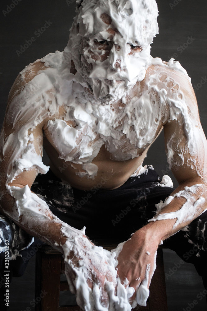 photo portrait of a muscular guy smeared with shaving foam sitting and leaning forward