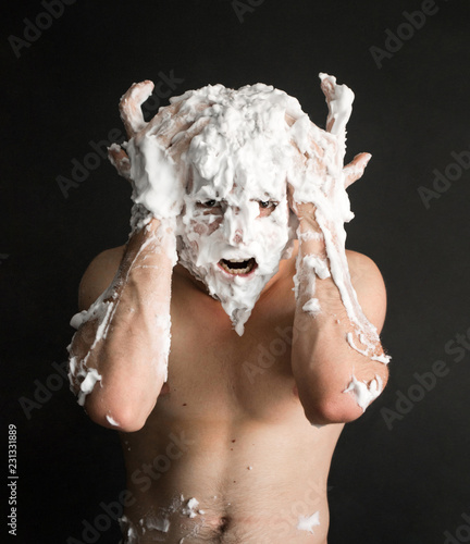 Fototapeta Naklejka Na Ścianę i Meble -  photo portrait of a muscular screaming man smeared with shaving foam with hands on his head like the horns of a buffalo