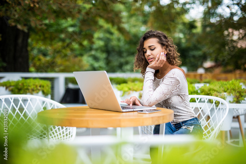 Taking advantages of free Wi-Fi. Beautiful young curly latin woman working on laptop and smiling while sitting outdoors in cafe © F8  \ Suport Ukraine