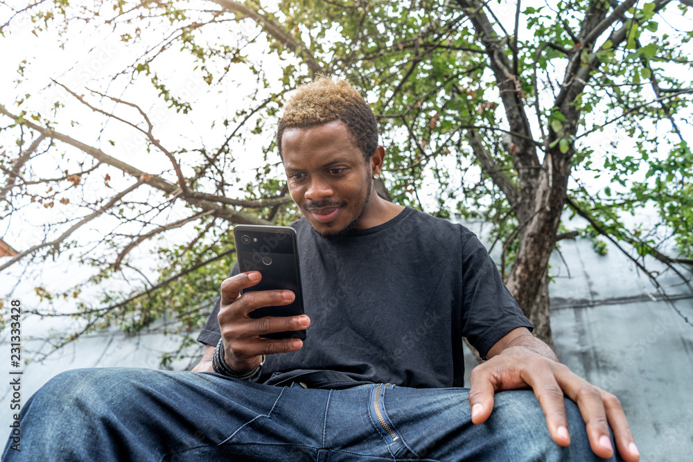 Pensive dark-skinned man in black T-shirt looking at mobile phone screen. Pensive dark-skinned man in black T-shirt looking at mobile phone screen.