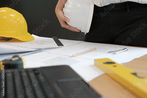 engineer architect worker holding safety helmet hardhat wtih construction blueprint on desk