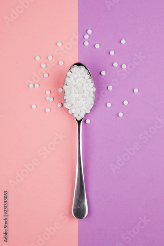 Sugar-replacing tablets with a spoon on a pink and purple background