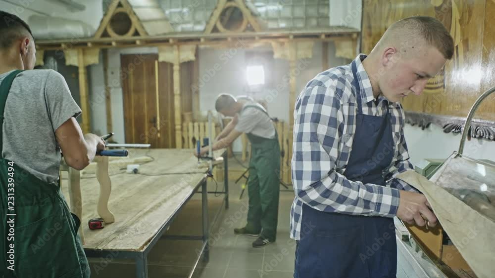 View of men working with wood in light spacious joinery shop illuminated with lamps. View of men working with wood in light spacious joinery shop illuminated with lamps.