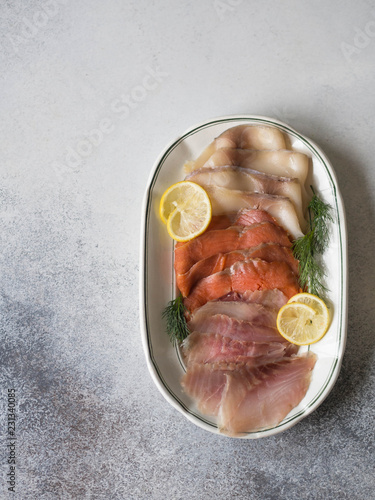 Slices of various salted fish - salmon, muksun, oily fish on an oval white plate on a gray background. Top view. Copy space photo