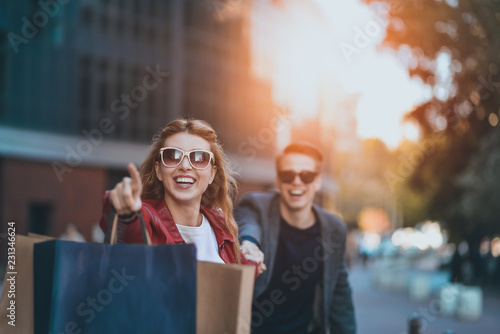 фотографія Front view of a casual couple of shoppers running in the street towards camera holding colorful shopping bags