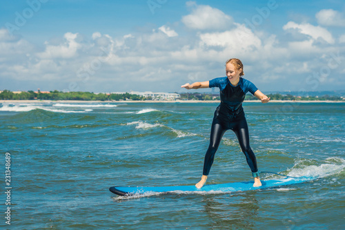 Canvas Print Joyful young woman beginner surfer with blue surf has fun on small sea waves