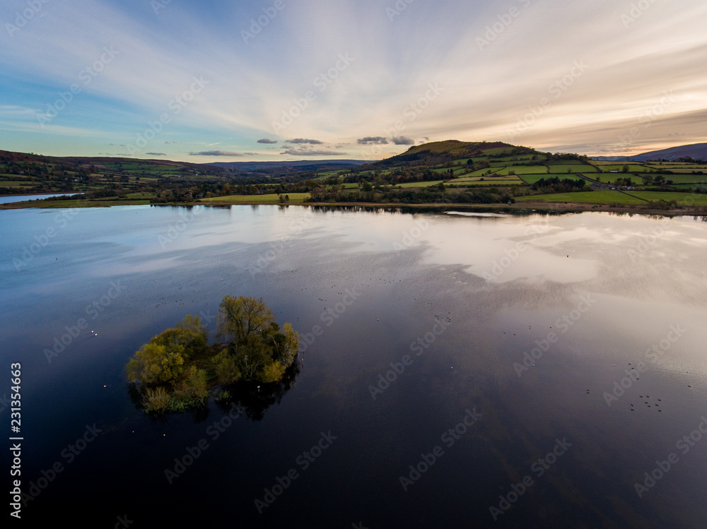 Fototapeta premium Aerial panoramic view of a beautiful natural lake in Brecon Beacons surrounded by rural farmland (Llangorse Lake, Wales)