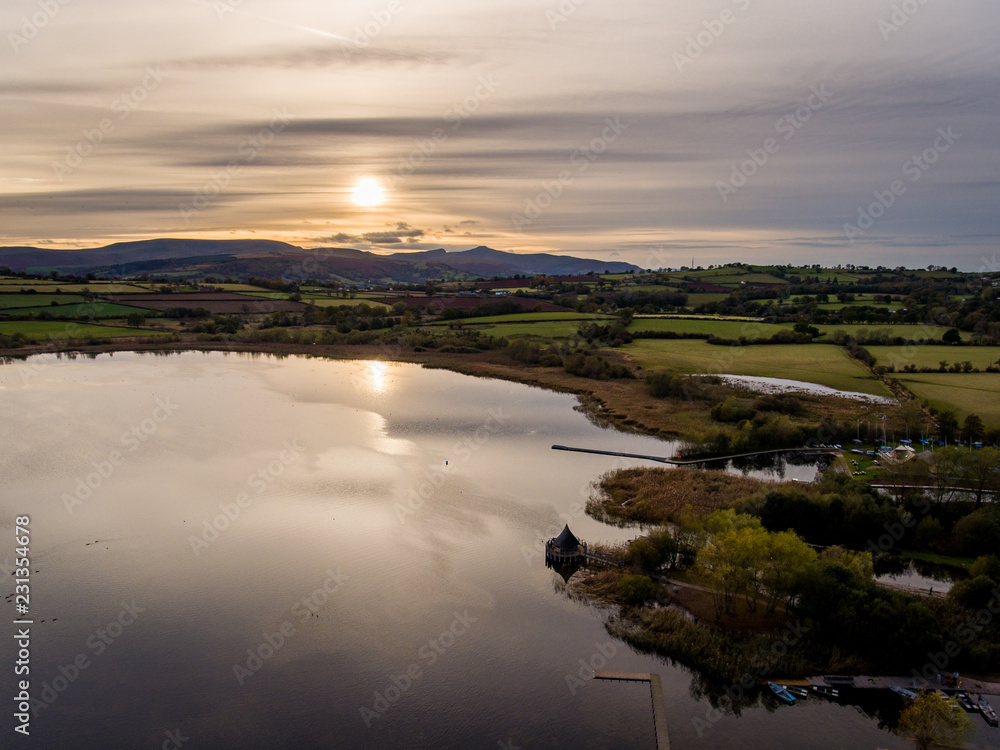 Aerial panoramic view of a beautiful natural lake in Brecon Beacons surrounded by rural farmland (Llangorse Lake, Wales)