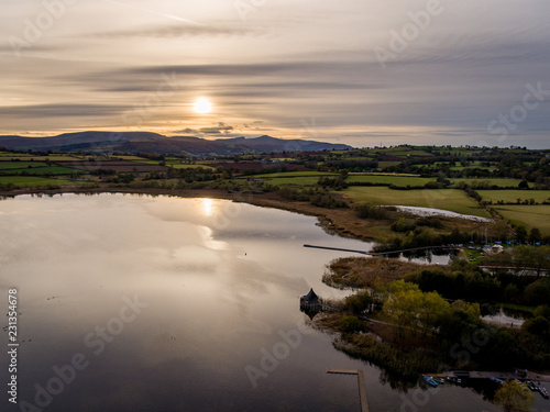 Aerial panoramic view of a beautiful natural lake in Brecon Beacons surrounded by rural farmland (Llangorse Lake, Wales)