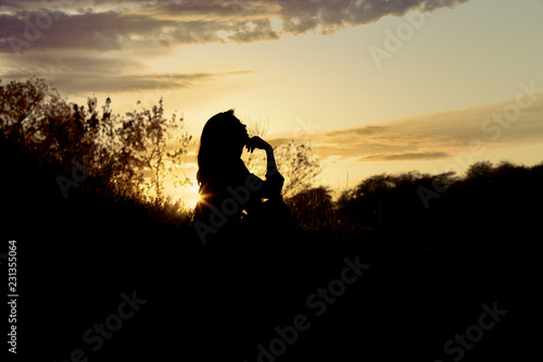 silhouette of a young woman sitting on a hill at sunset, a girl walking in the autumn in the field