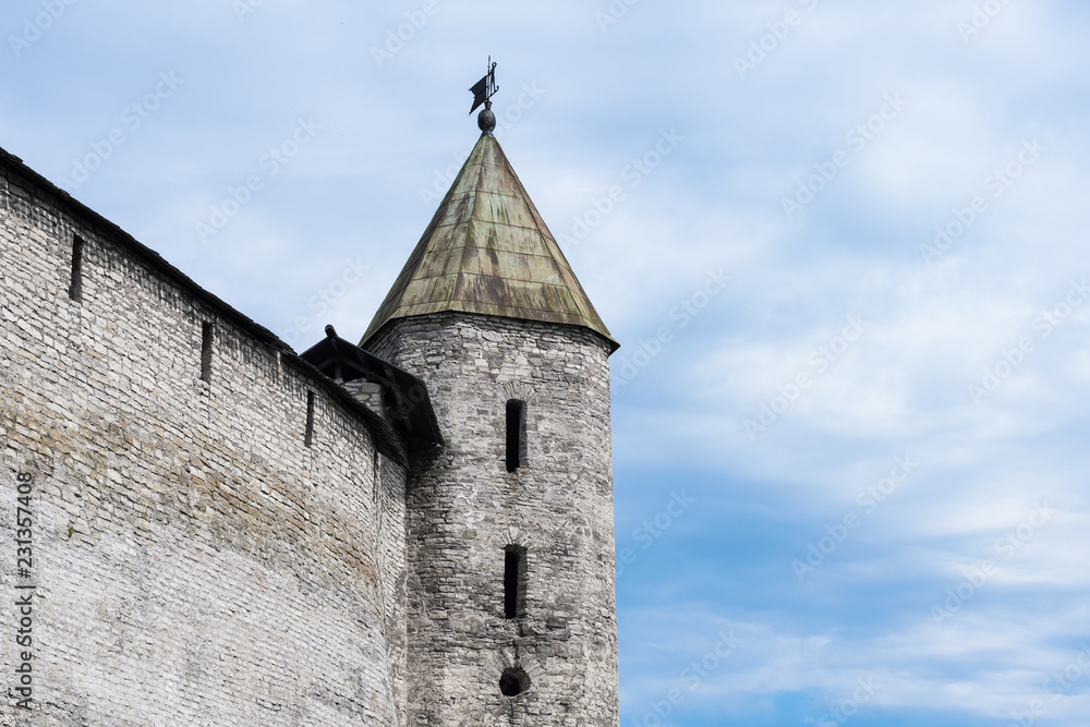 Part of a fortified wall with a tower on the background of a cloudy blue sky