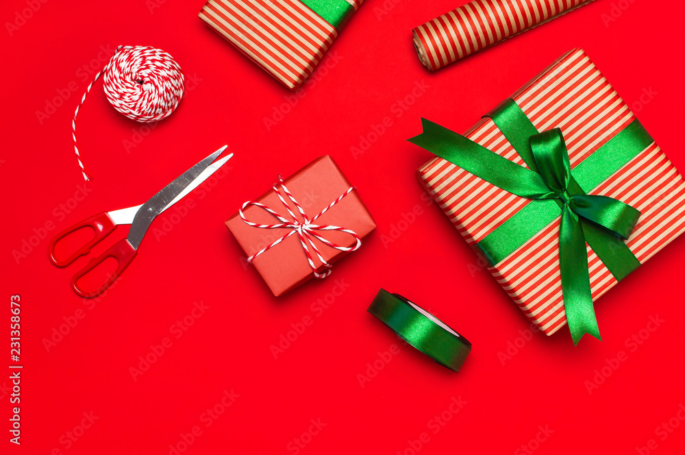Gift boxes, packing paper, scissors, ribbon on red background