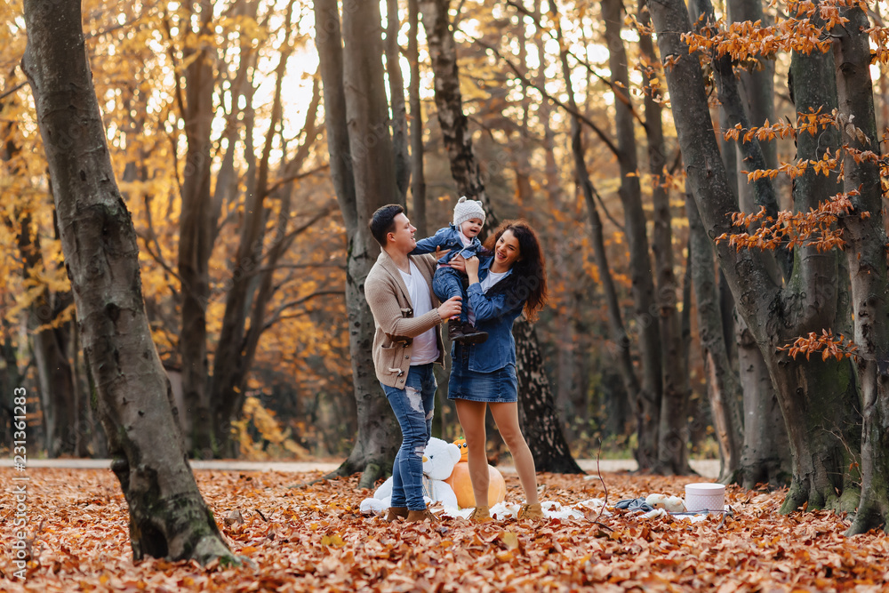 happy family with little cute child in park on yellow leaf with big pumpkin in autumn