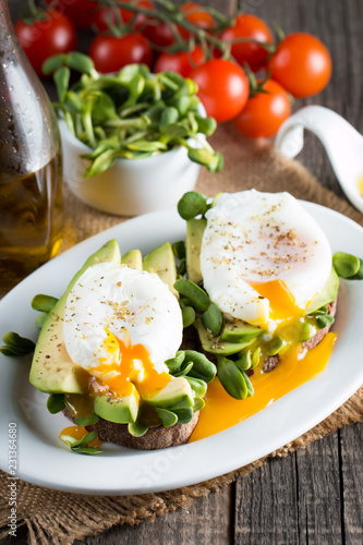 Avocado toast, cherry tomato on wooden background. Breakfast with toast avocado, vegetarian food, healthy diet concept. Healthy sandwich with avocado and poached eggs.
