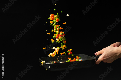 Flying mixed vegetables in a pan. Diet healthy food. Black background for copying text. Concept of food and cooking.