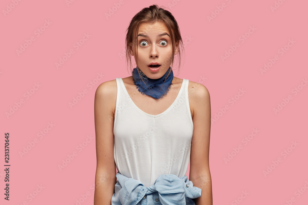 Waist up of startled overwhelmed Caucasian girl wears casual white vest, bandana around neck, shirt on waste, expresses and shock, models pink background. Reaction concept Stock Photo | Adobe
