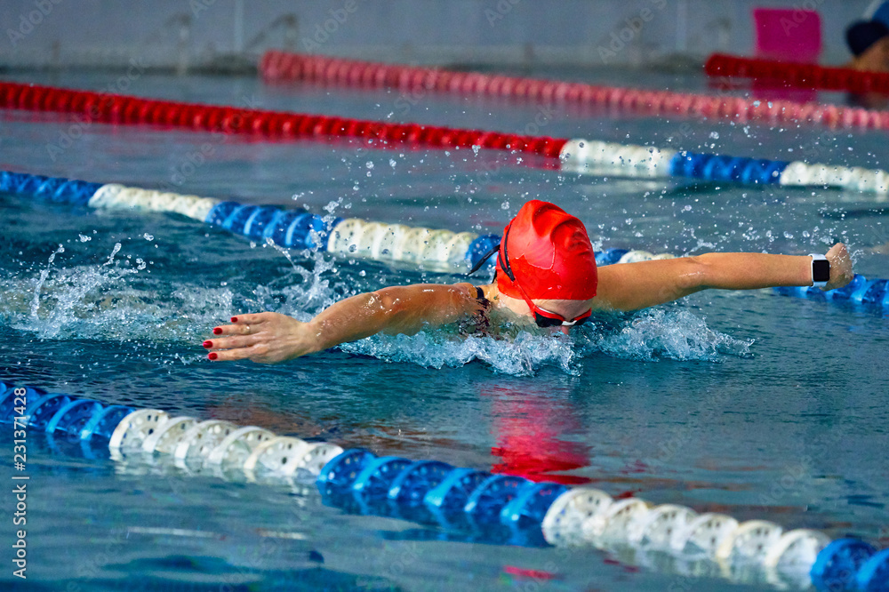 Female athlete swims with a butterfly style. Splashes of water scatter in different directions.