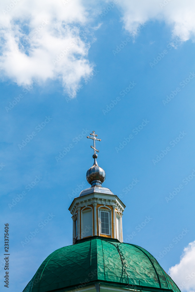 Green dome of a Christian temple with a cross against the blue sky with white clouds.