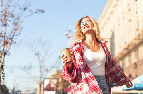 Smiling beautiful blonde womam walking at the street, holding cup of coffee. photo