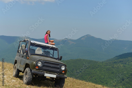 Teenage girl sitting on the roof of an SUV in the mountains in the summer. © Лариса Левина