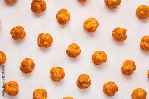 Assorted fresh cream puff cakes on rose background. Top view.