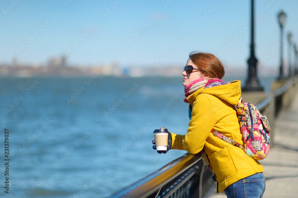 Happy young woman tourist sightseeing in New York City at sunny spring day. Female traveler drinking coffee in downtown Manhattan.