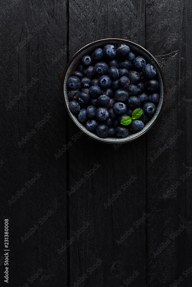 Top view of blueberries in a bowl with fresh mint leaf on black wooden background with copy space. Top view of blueberries in a bowl with fresh mint leaf on black wooden background with copy space.