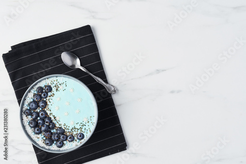 Top view of blue yogurt smoothie bowl made with blueberry, coconut flour, chia seeds and sugar pearls on white marble table with copy space. photo