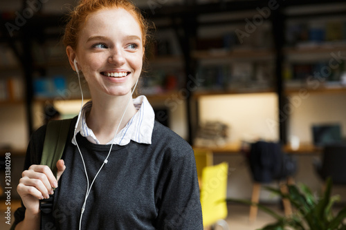Smiling younh teenage girl in earphones carrying backpack photo