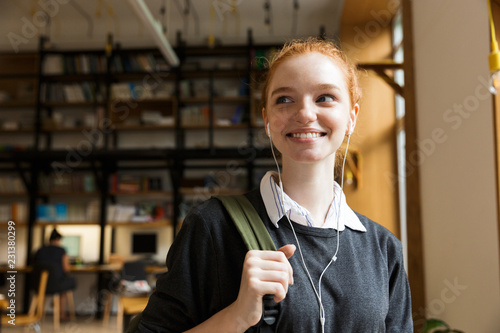 Redhead lady student posing indoors in library istening music with earphones. photo