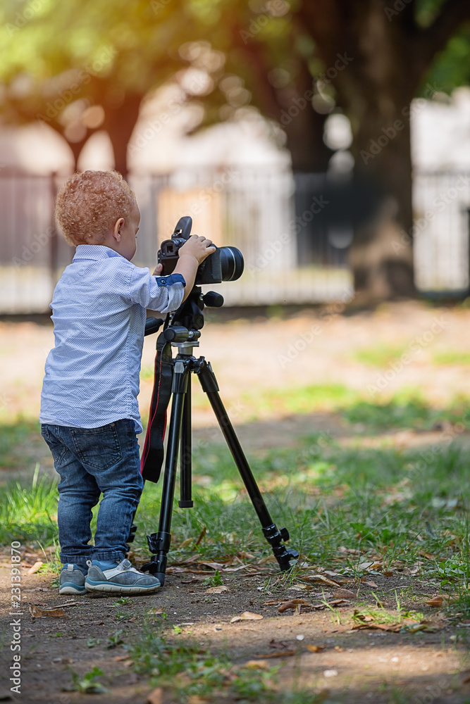 Little boy photographing on the camera on tripod in the park