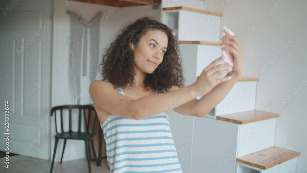 Young woman taking selfie by mobile phone in kitchen. Young woman taking selfie by mobile phone in kitchen.