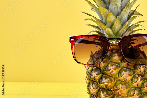Close up pineapple in sunglasses and copy space. Fresh hawaiian pineapple wearing sunglasses on yellow background with text space.